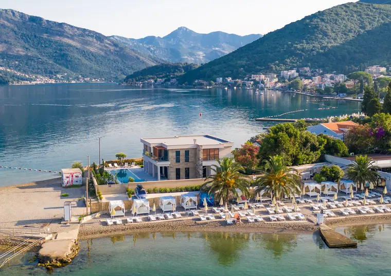 The waterfront terrace and beach, with sun loungers in rows behind a low sea wall and boats moored offshore.