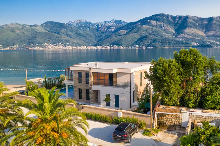 The villa from the south-west, palms in the foreground and the bay beyond.