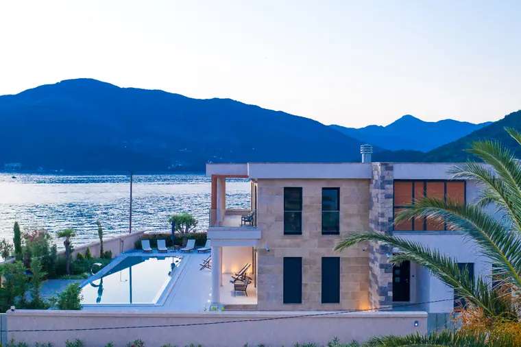 The villa and its lit terrace from the south, the pool running parallel to the shore.