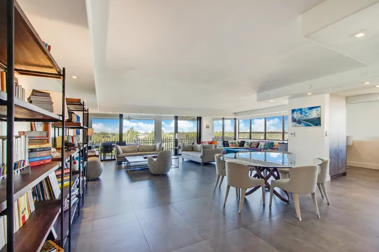 The main living space seen from the entrance, with a full-height shelving wall, dining table and glazing beyond.