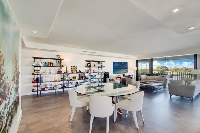 The dining area, with a round glass table and a shelving wall holding books and objects.