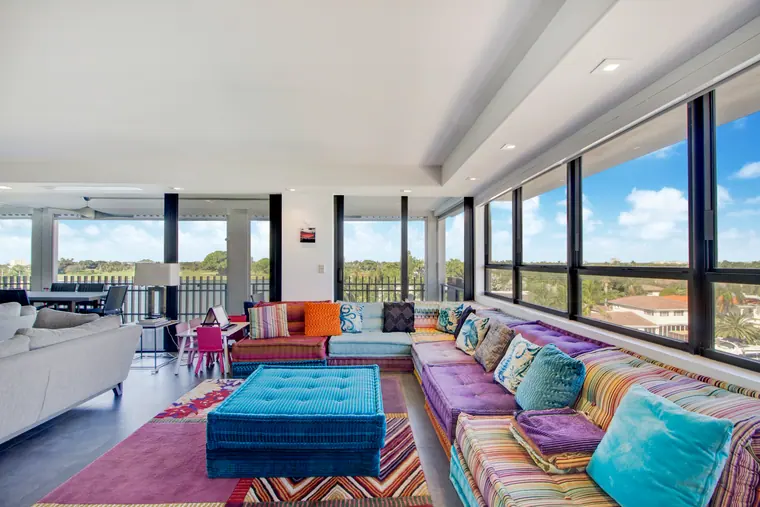 The living room, with a patterned rug, upholstered ottoman and sofas beneath continuous glazing.