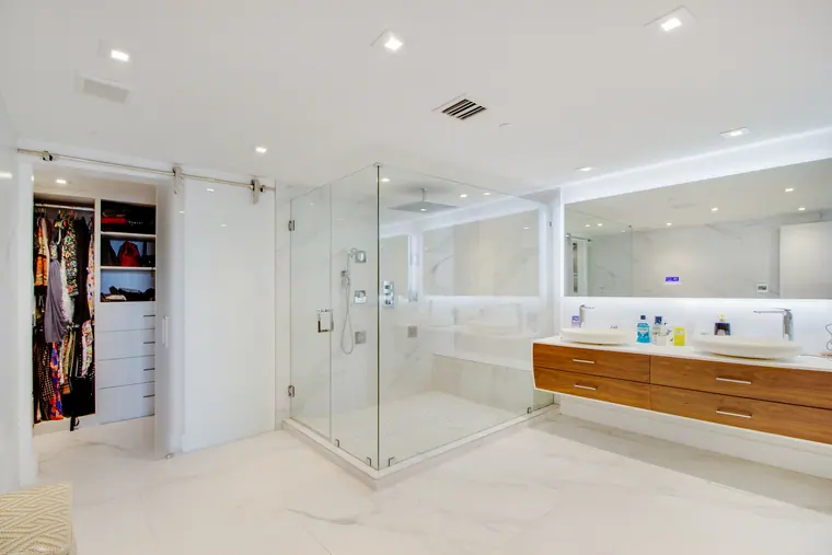 The main bathroom: glazed shower, twin vanity in timber and stone, and a walk-in wardrobe beyond.